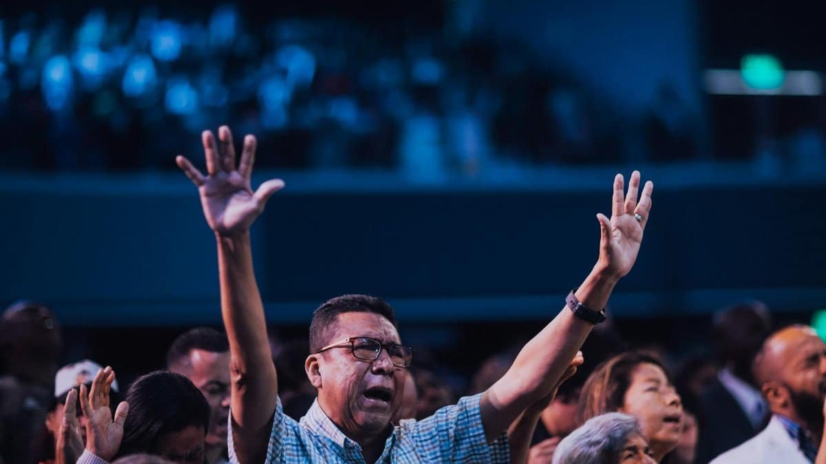 Diverse group of people engaging in worship with hands raised indoors.