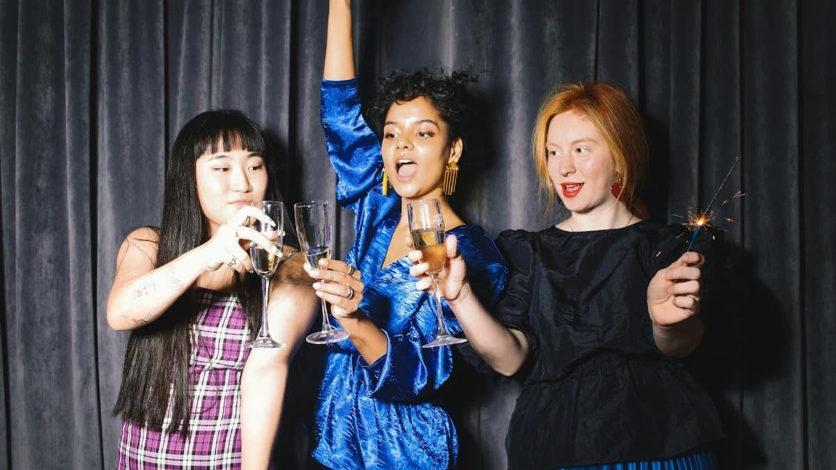 Three women celebrating with wine and sparklers in a festive indoor setting.