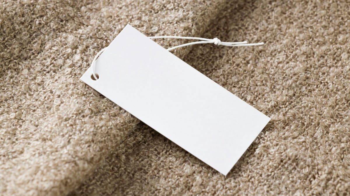 Close-up of a blank white price tag on textured beige fabric, ideal for branding use.