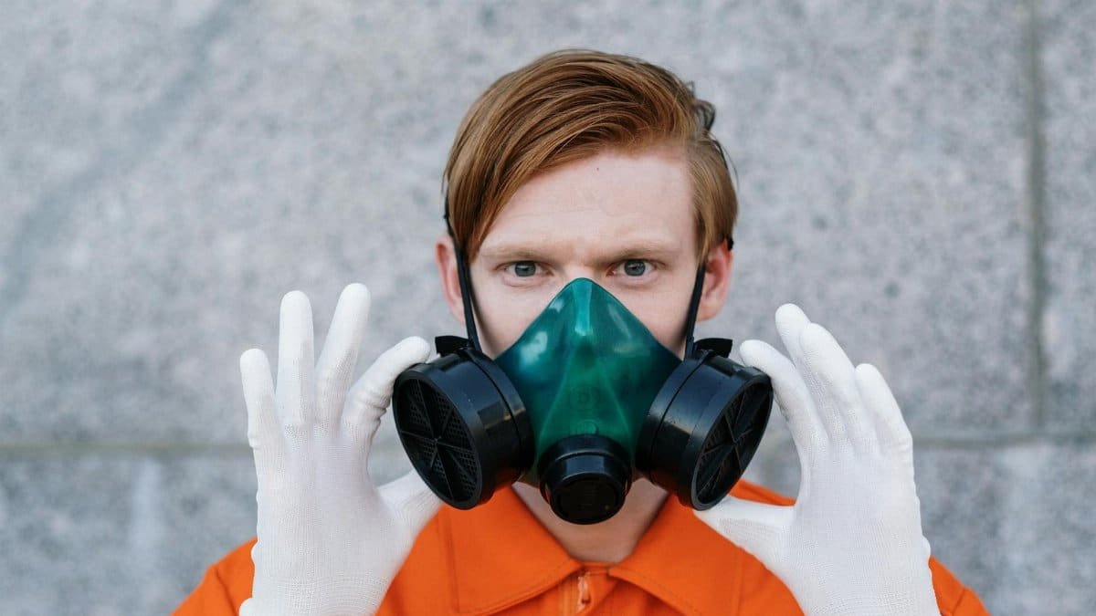 A young adult wearing a respirator mask and gloves for safety against toxins or pollutants.