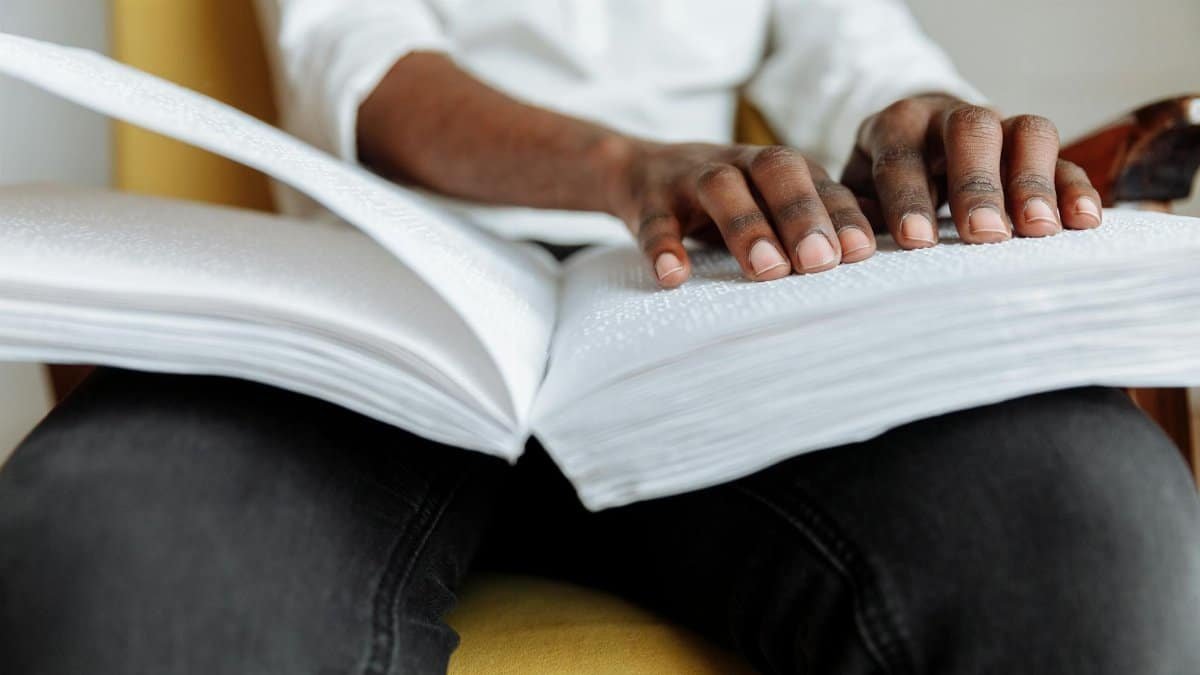 Close-up of a person reading a Braille book indoors, focusing on hand movement.