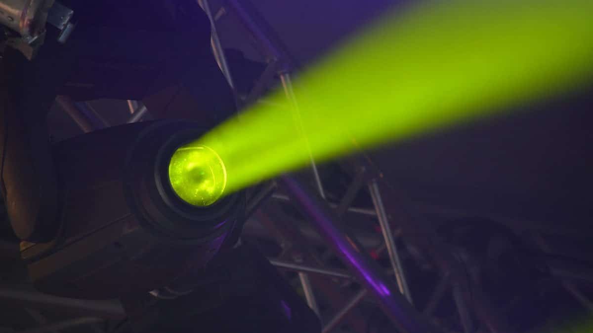 Close-up of a vivid neon spotlight emitting a green beam, part of modern stage lighting equipment.