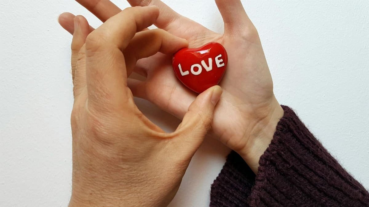 Two hands holding a red heart with the word 'love' on a white background.