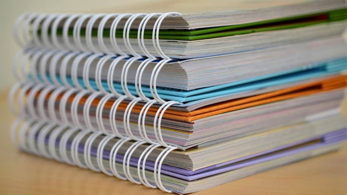 A colorful stack of spiral-bound notebooks neatly placed on a wooden desk. Ideal for educational themes.