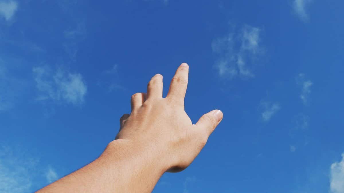 A human hand reaching toward a bright blue sky, symbolizing freedom and aspiration.