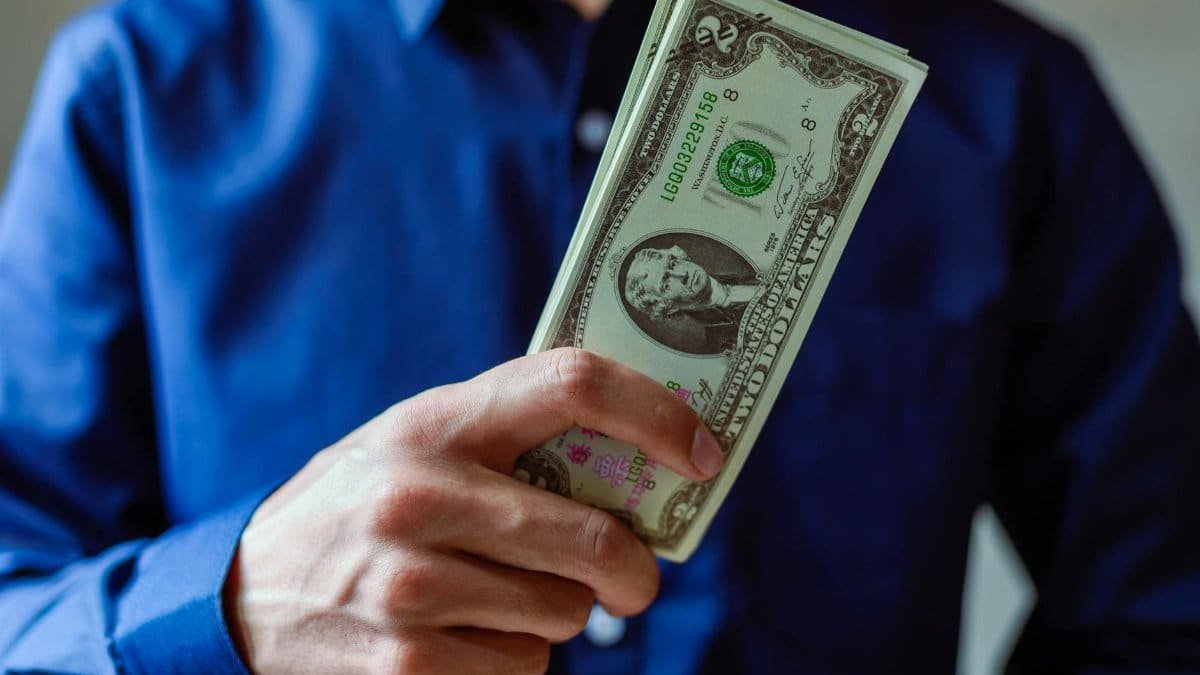 Close-up of a person holding two dollar bills, representing wealth and finance.