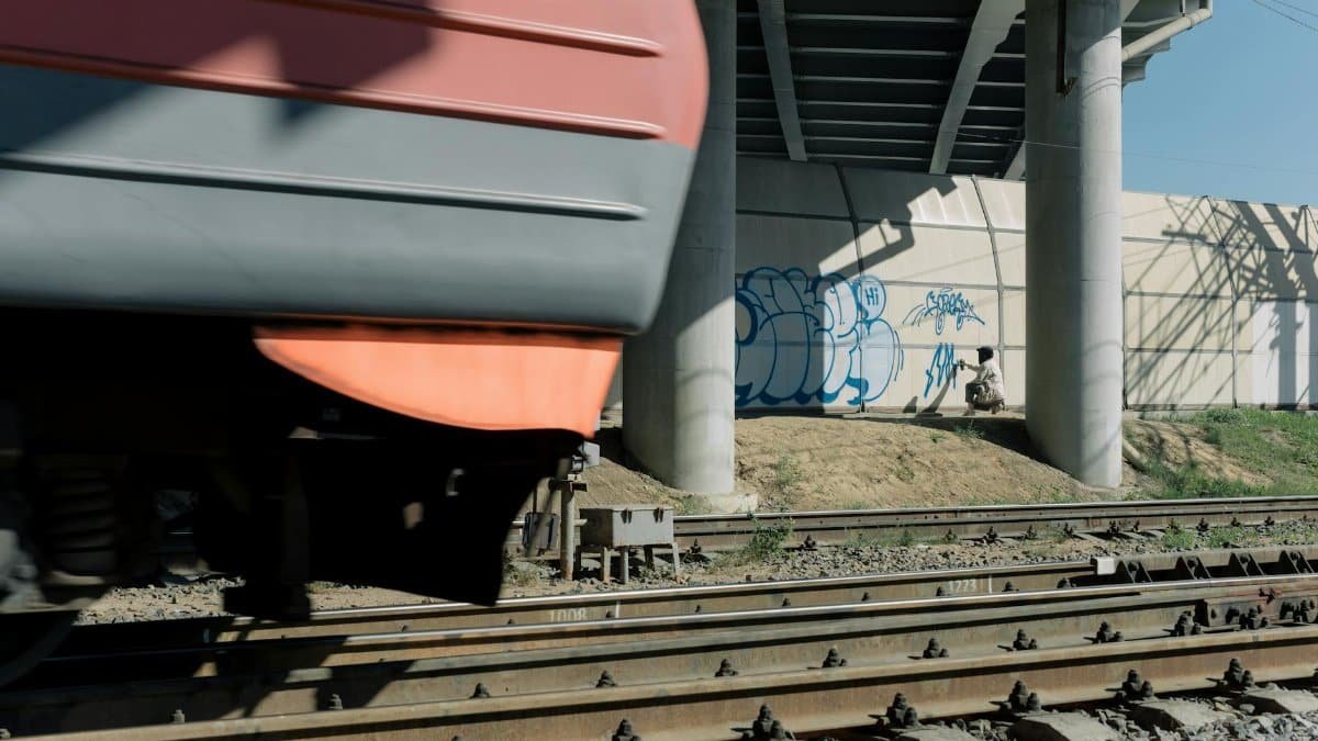 Train speeding under a graffiti-covered bridge with visible railway tracks and vibrant street art.