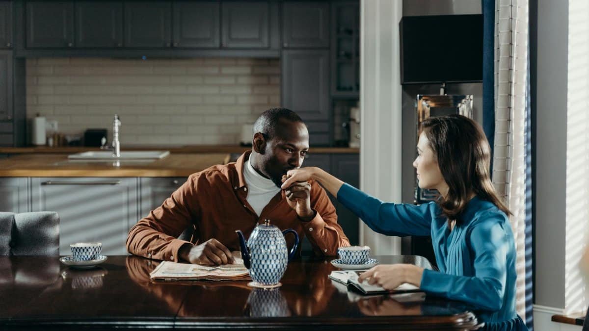 A romantic couple sharing a moment over tea at a wooden table in a cozy kitchen.