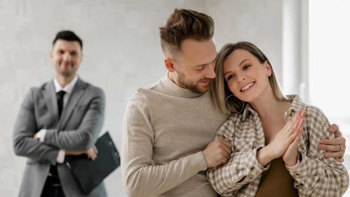 Smiling couple with real estate agent celebrating new home purchase indoors.