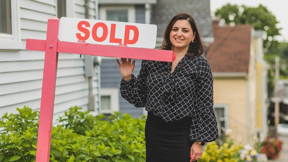 Smiling real estate agent standing outdoors with a sold sign, symbolizing success and achievement in property sales.