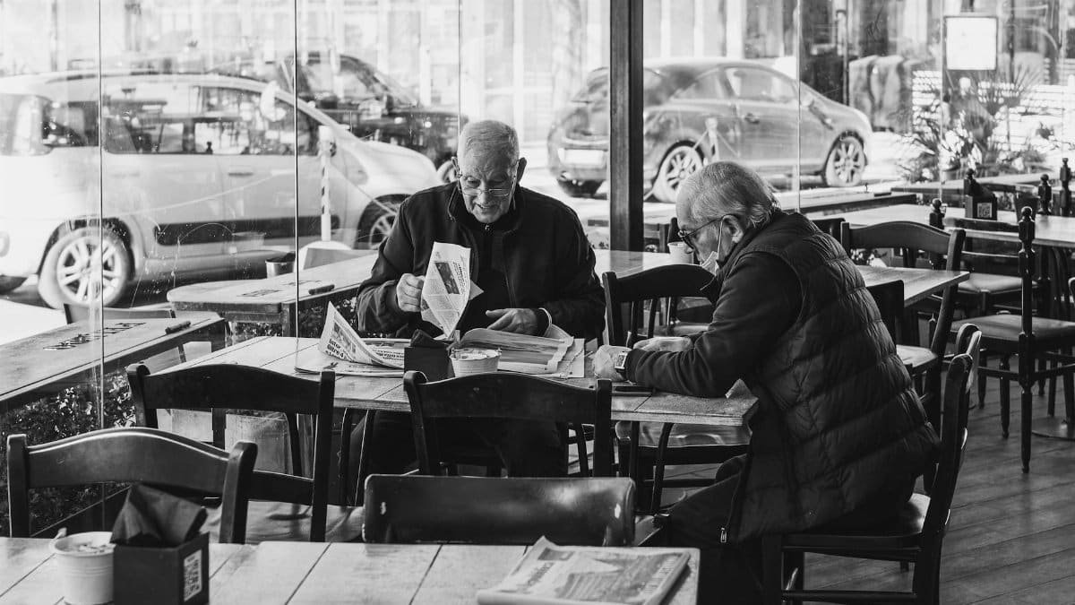 Two senior adults reading newspapers in a Rimini cafe, Italy.