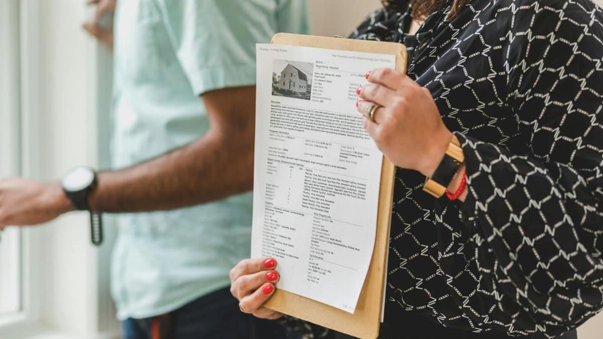 Real estate agent holding property documents on a clipboard in an office setting.