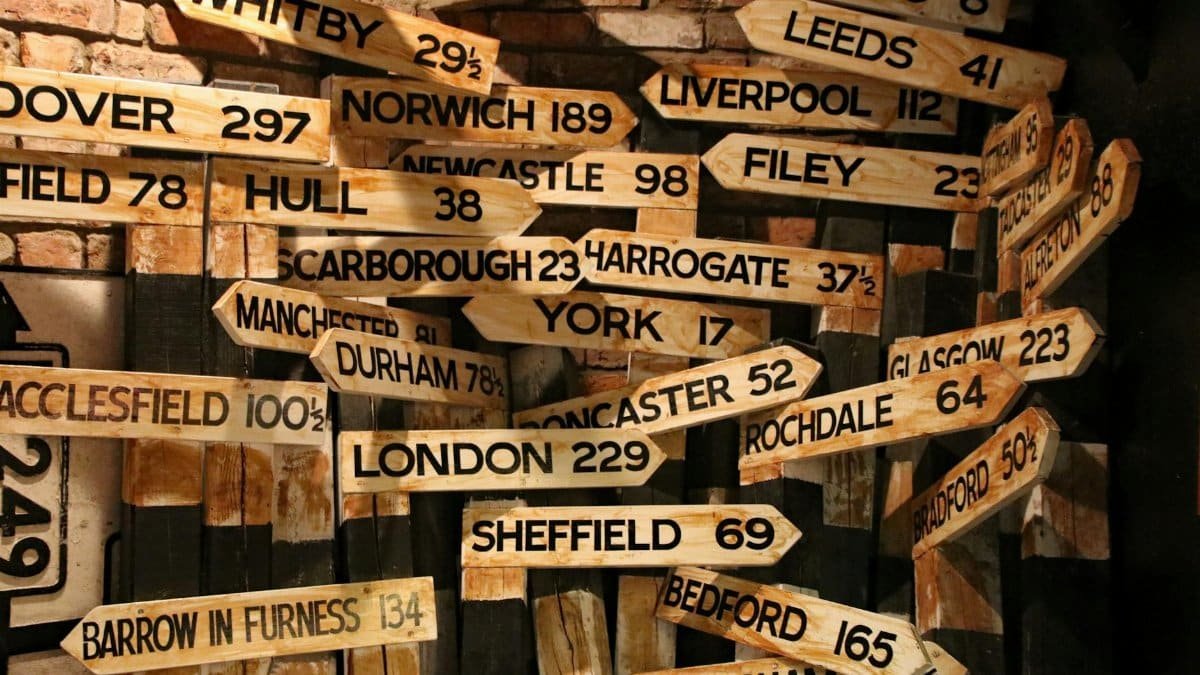 A collection of vintage wooden road signs showing distances to various UK towns and cities.