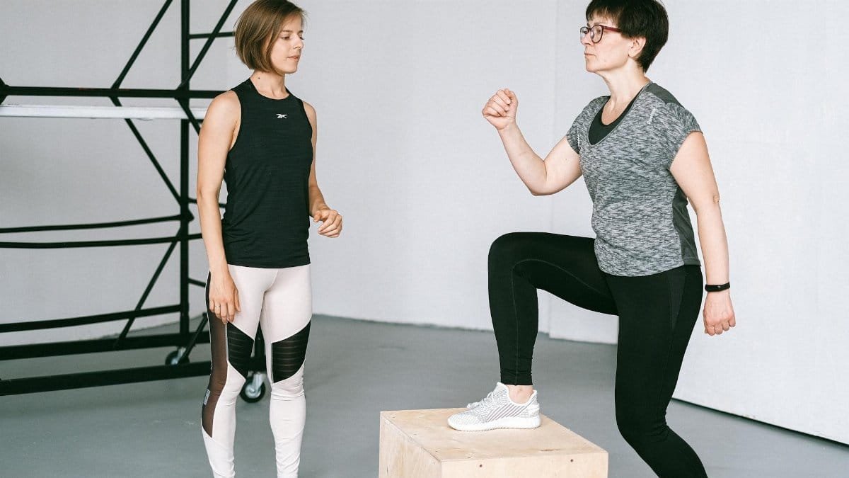 Fitness coach guides a woman in workout indoors. Focus on exercise and healthy lifestyle.