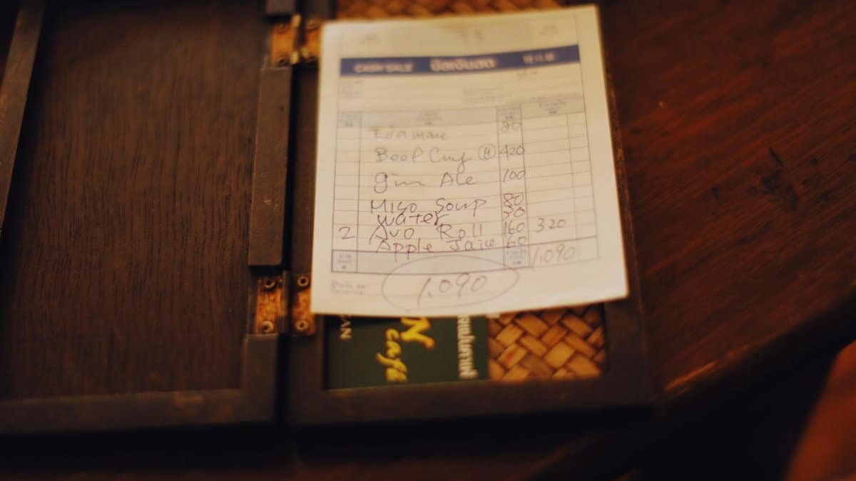 Close-up of a restaurant bill placed on a dark wooden table, creating a moody ambiance.