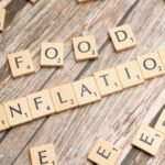 Wooden scrabble tiles arrange to spell 'Food Inflation' on a rustic wooden surface, conceptually depicting rising food prices.
