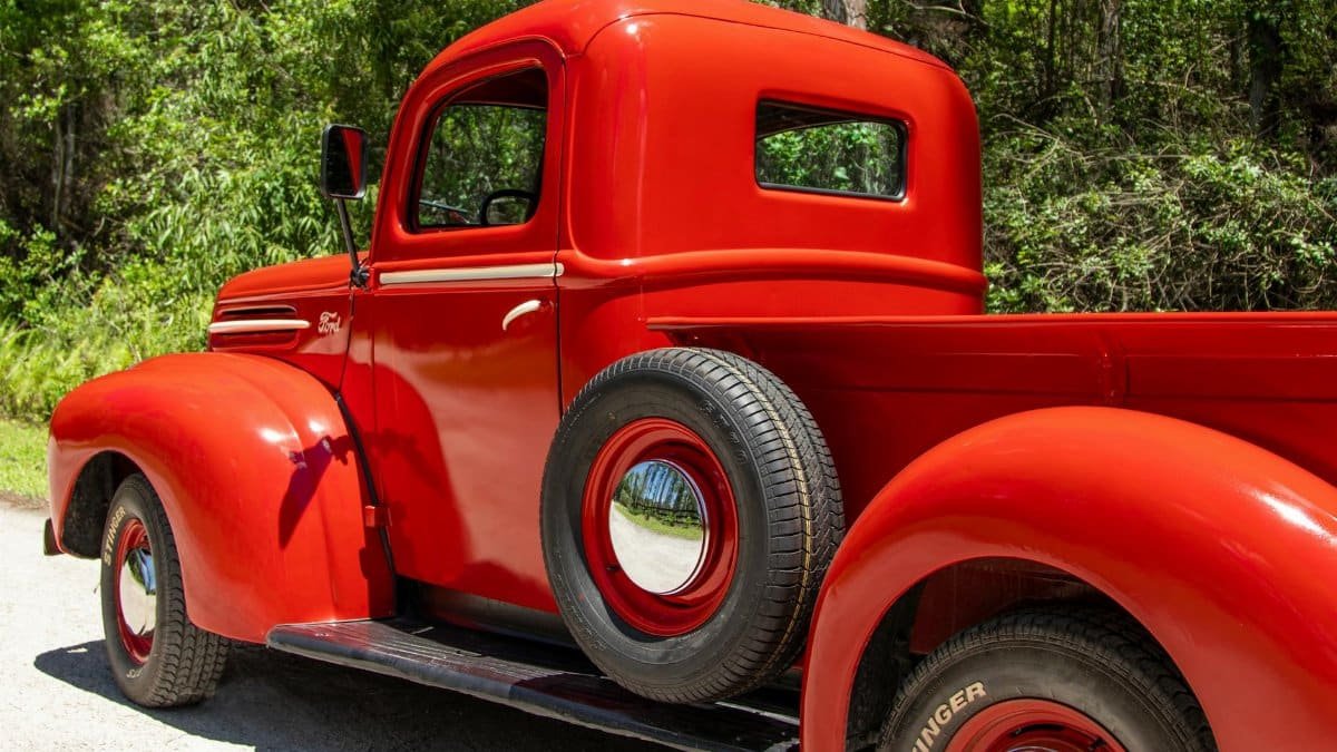 Restored vintage red Ford truck parked on a sunny day surrounded by nature.