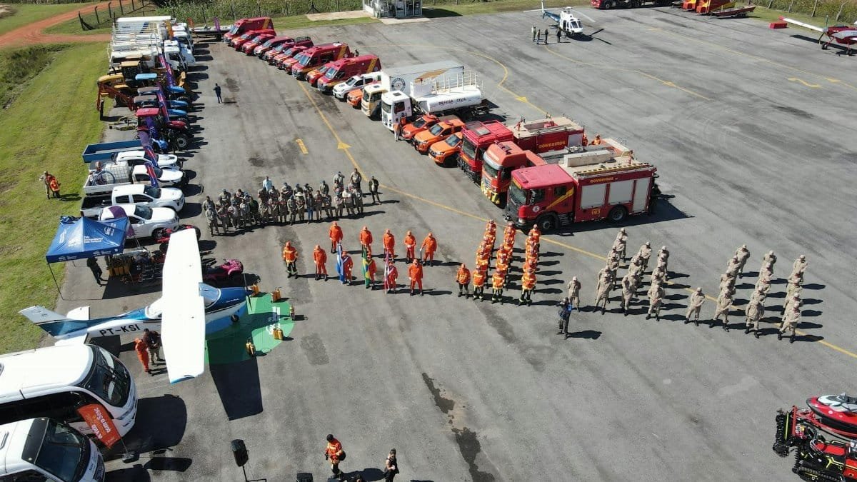 Aerial shot of fire trucks, emergency vehicles, and personnel in a training exercise. Clear day overview.