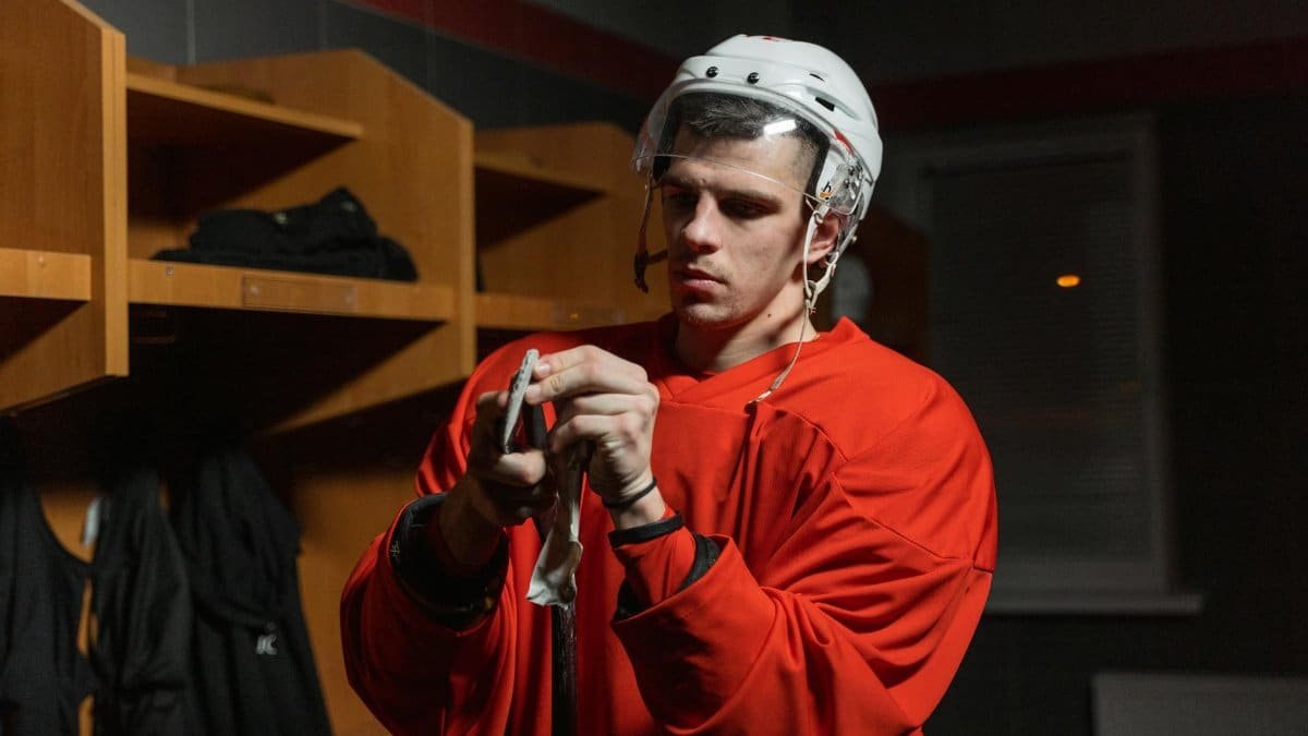 Male hockey player in locker room preparing stick, deep in focus.