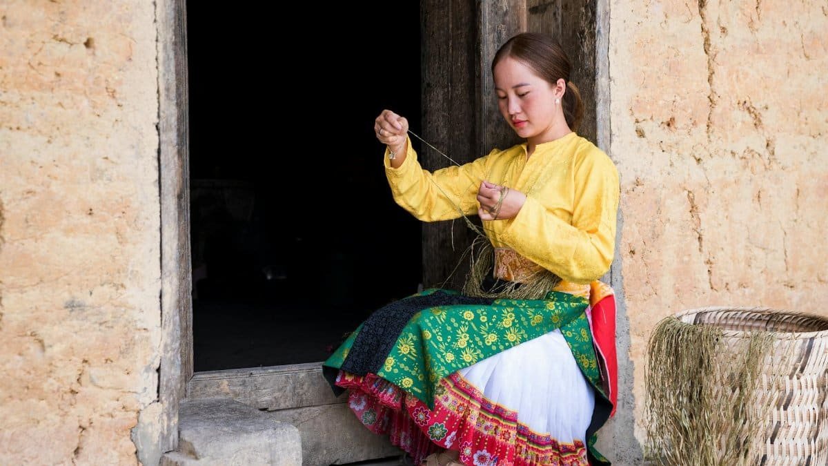 A woman in traditional attire weaving outdoors, showcasing cultural heritage and craftsmanship.