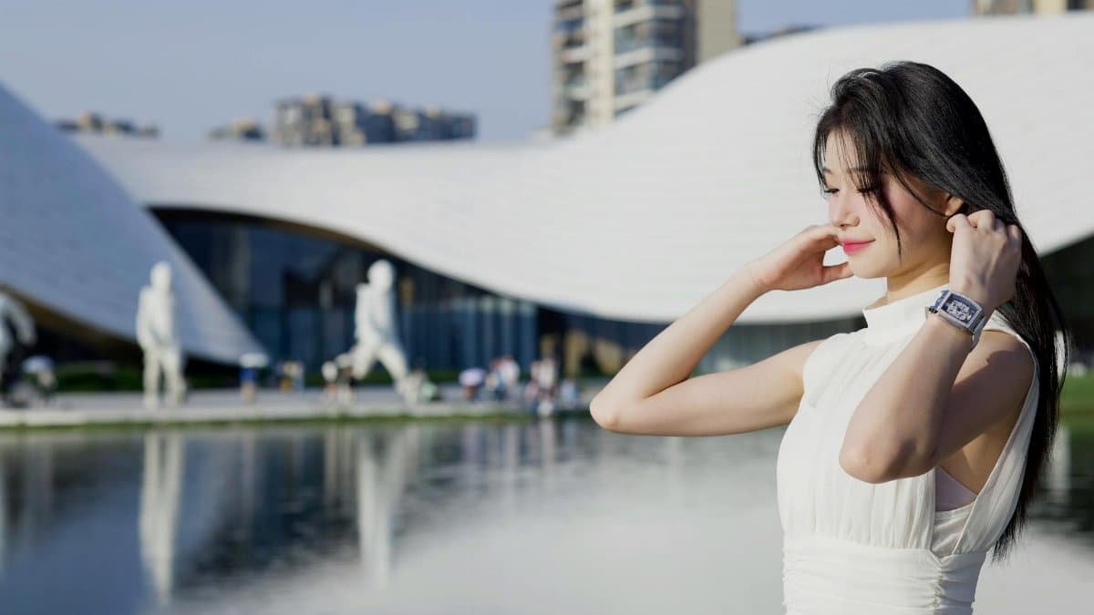 A stylish woman in Chengdu, China, poses by modern architecture with a serene pond reflecting the scene.