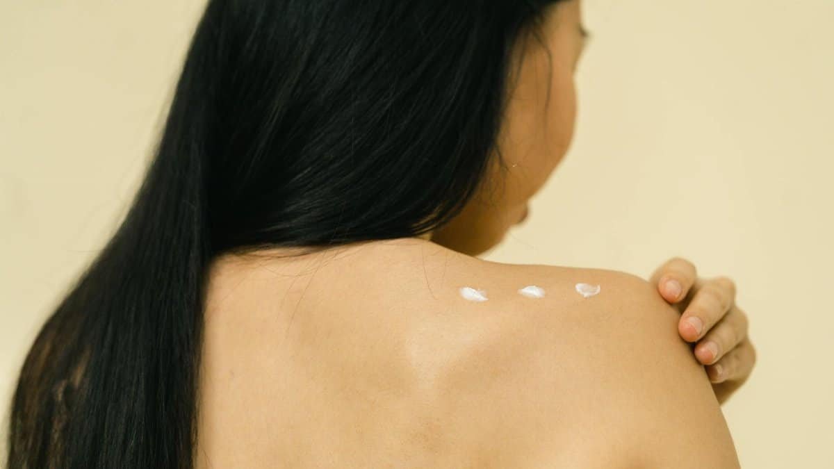 Close-up of a woman applying skincare cream on her shoulder in a studio setting.