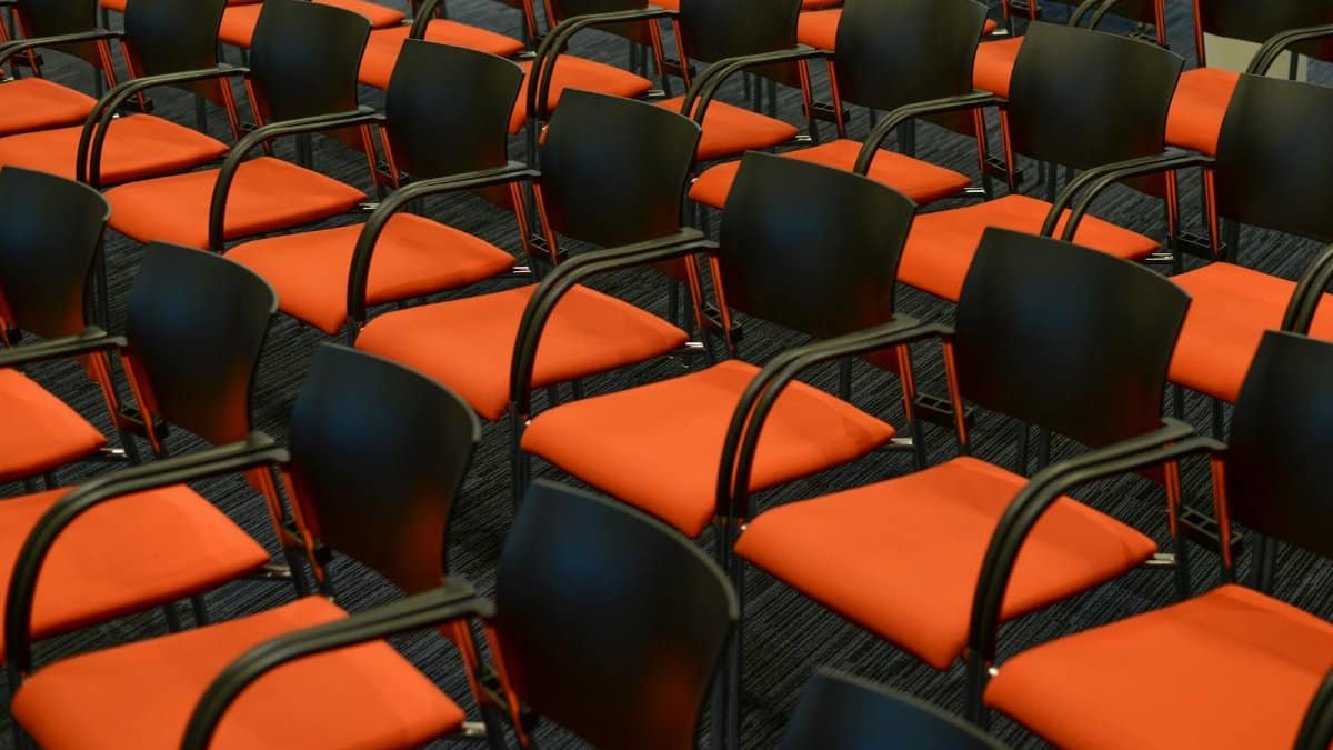 A modern auditorium with rows of empty black and orange chairs, ready for an event.