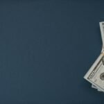 A bundle of US dollar bills on a dark blue background with ample copy space.