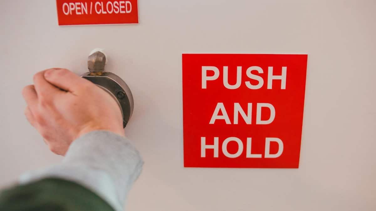 Close-up of hand operating knob with red safety signs 'OPEN/CLOSED' and 'PUSH AND HOLD'.