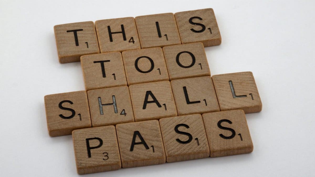 Wooden tiles form the motivational message 'This too shall pass,' highlighting resilience.