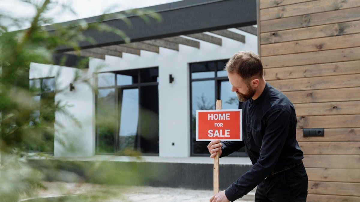 Man placing a home for sale sign outside a modern house for real estate listing.