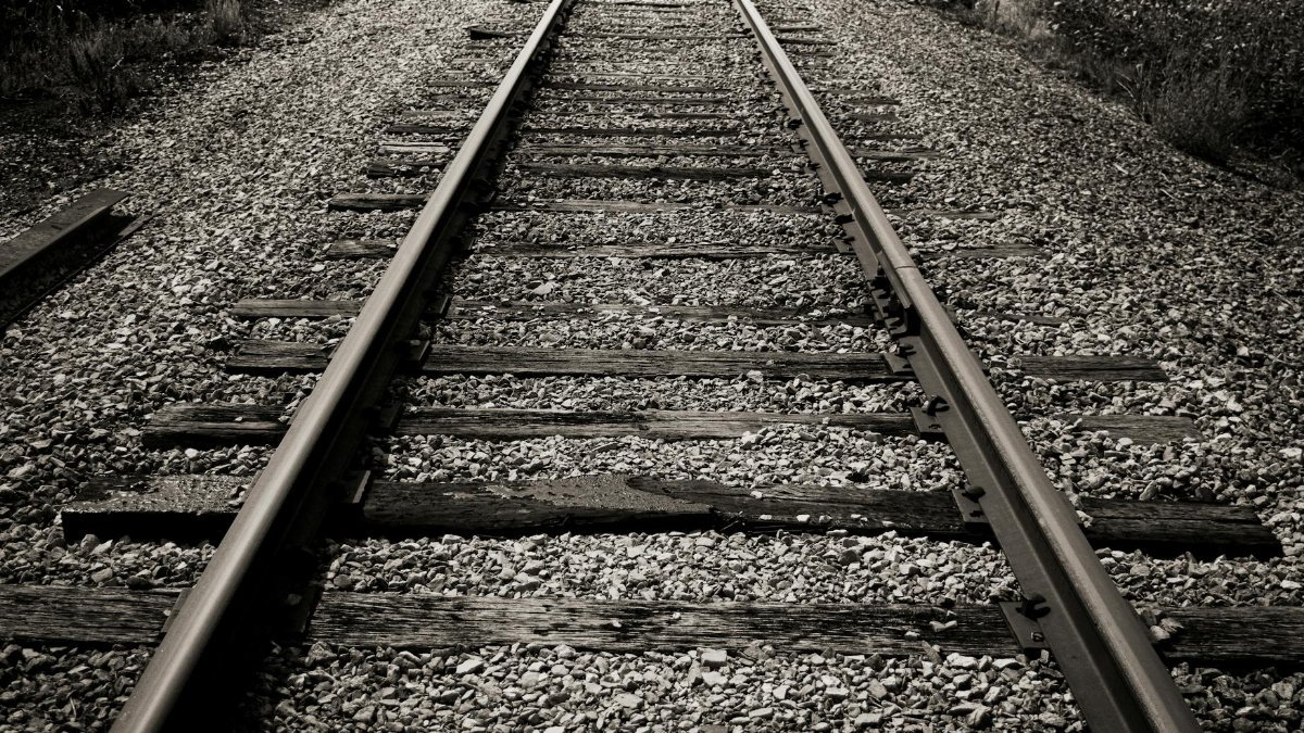 Black and white photo of rustic railroad tracks disappearing into the distance.