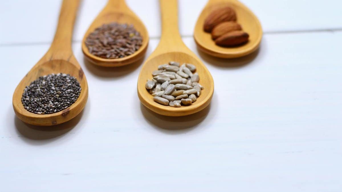 Close-up of various nuts and seeds in wooden spoons on a white background, showcasing healthy food options.