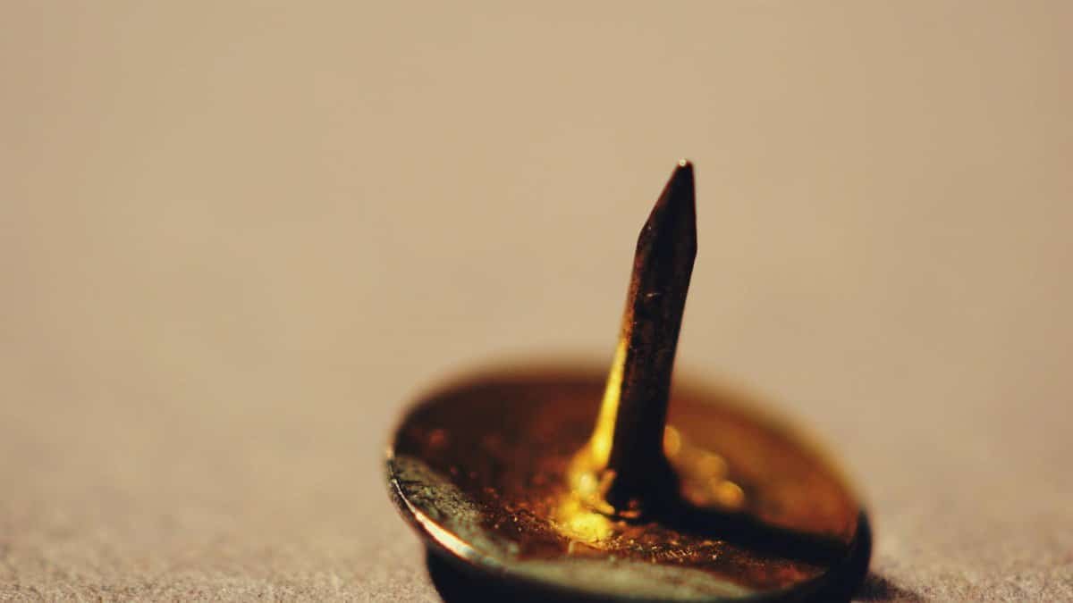 Sharp golden thumbtack standing upright on a blurred soft surface, macro perspective.