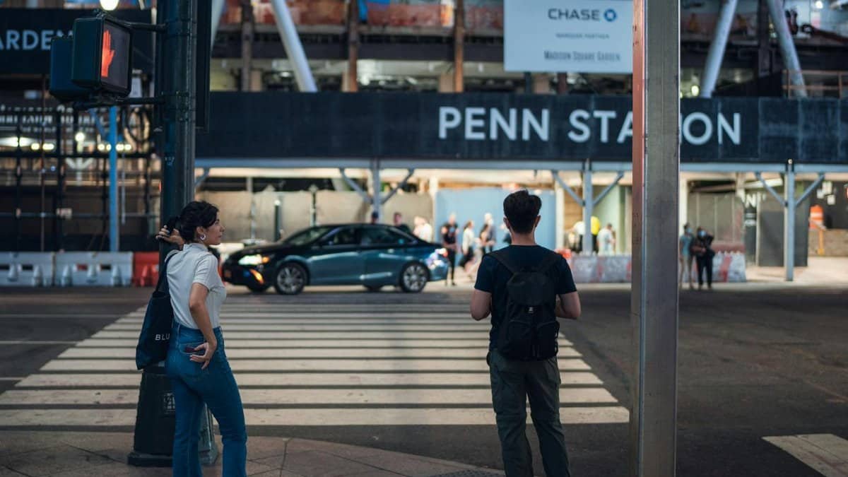 Two people wait at a pedestrian crossing near Penn Station in New York City, capturing urban life.