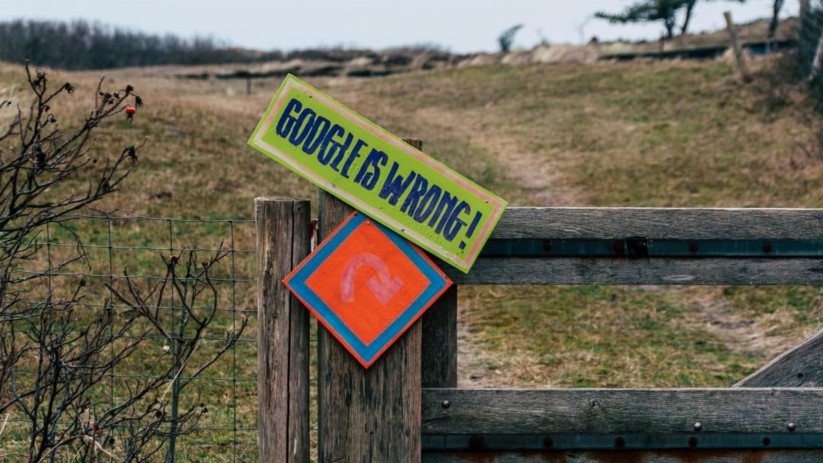 A wooden gate with humorous signs set in a rural landscape, expressing playful dissent.