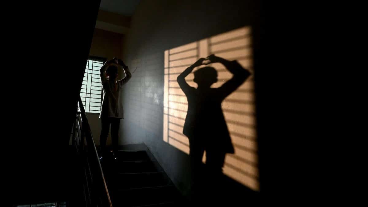 A person creates a silhouette on a stairway with dramatic shadows from a window.