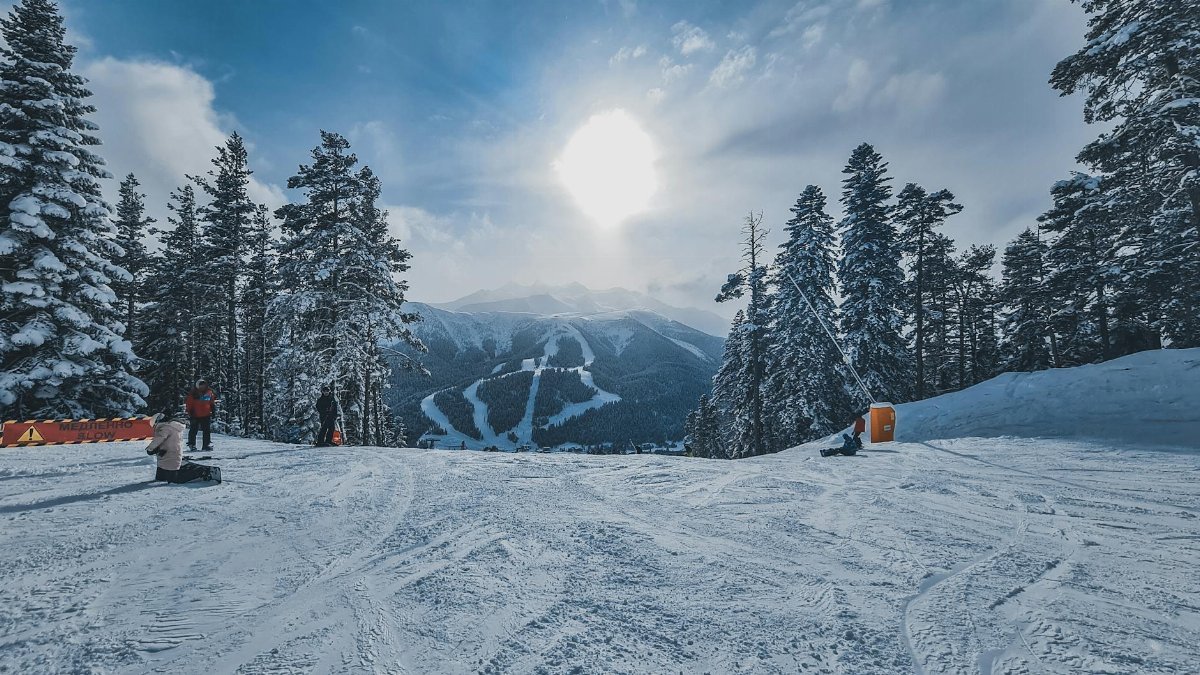 A sunny day at a ski resort with snow-covered mountains and pine trees.