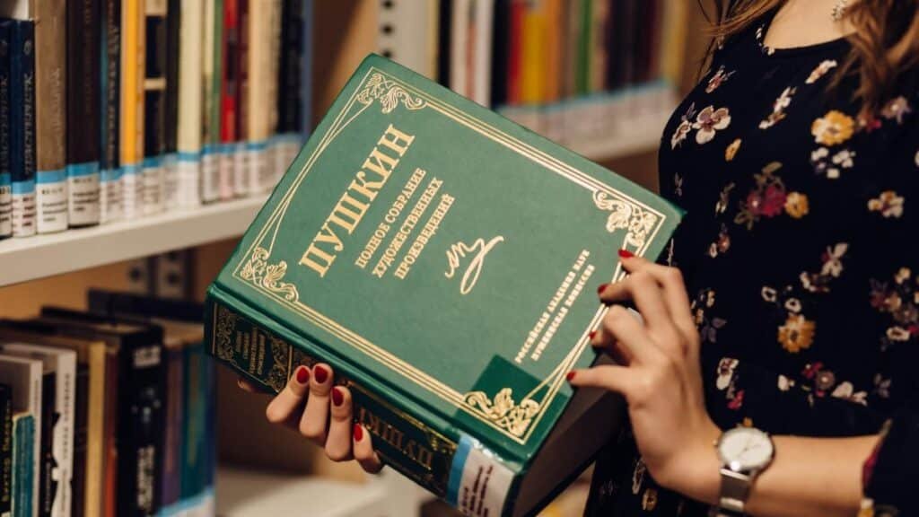 A woman holds a Russian literature book in a library, showcasing a focused study environment.
