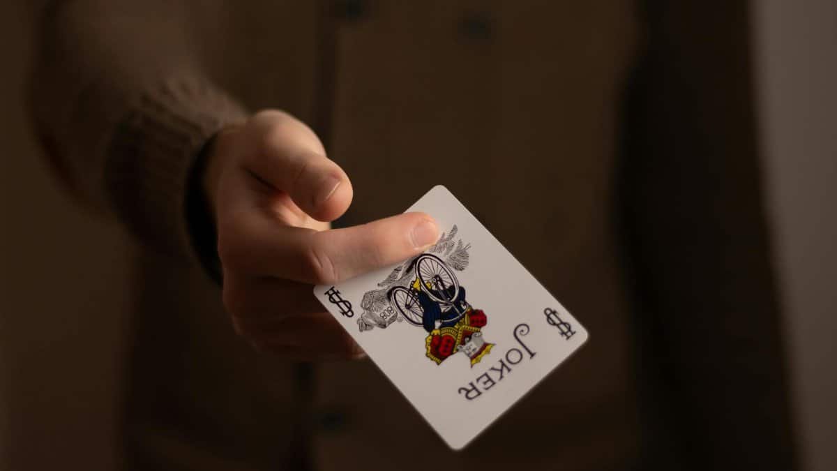 A close-up image of a hand holding a joker playing card, emphasizing gambling theme.
