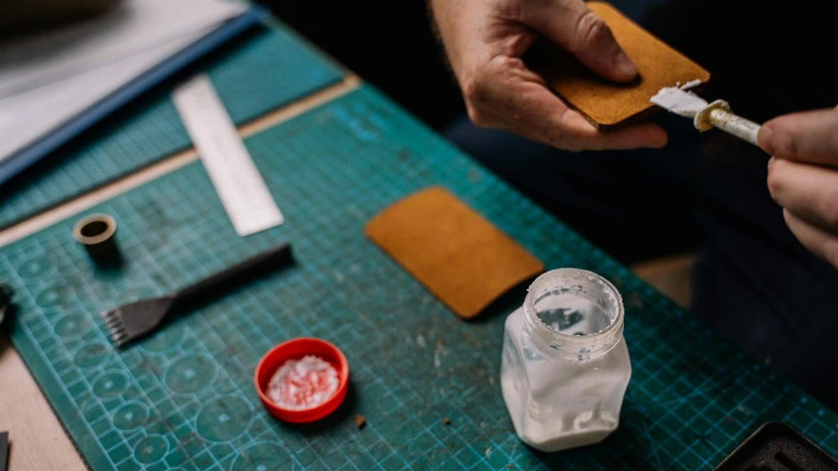 A detailed close-up of a person applying glue on leather for crafting purposes, showcasing handwork and tools.