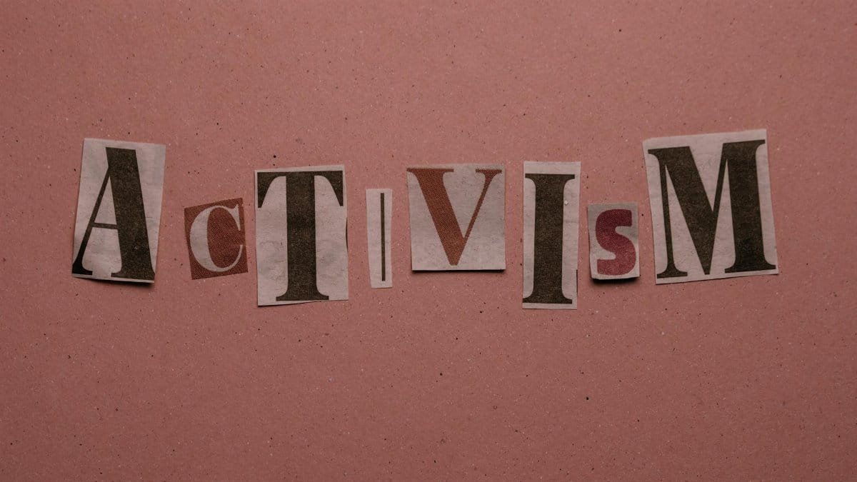 Paper cutouts spelling 'Activism' on a pink surface, emphasizing social movement themes.