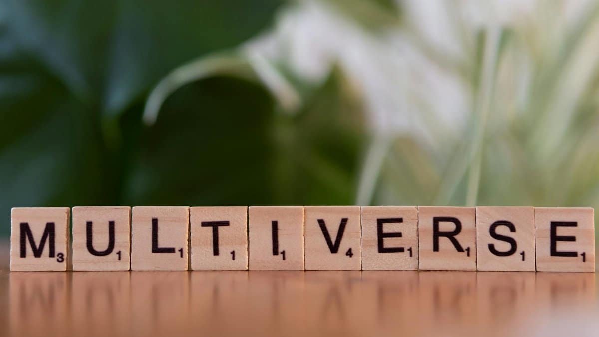 Wooden Scrabble tiles spelling multiverse against a blurred leafy background.