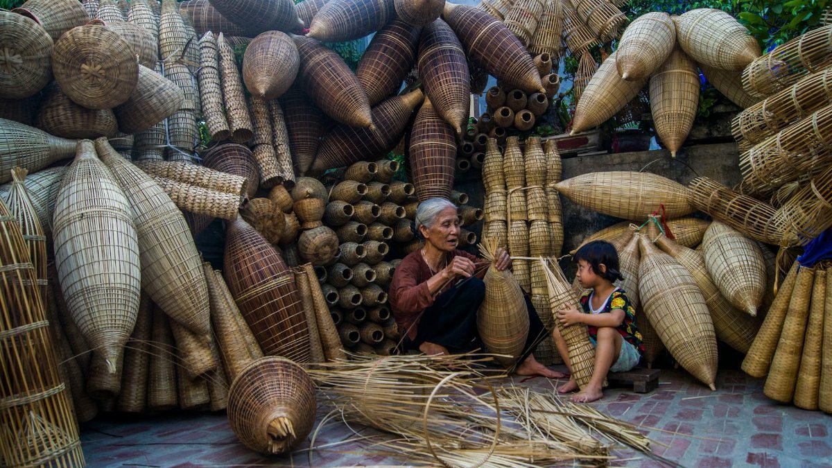 Elderly woman and child weaving traditional wicker baskets surrounded by artisan craftsmanship.