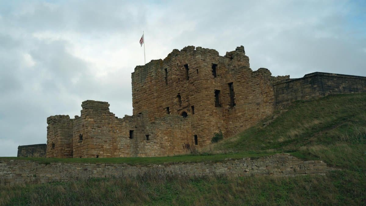 A beautiful view of ancient castle ruins set on a grassy hill under a cloudy sky.