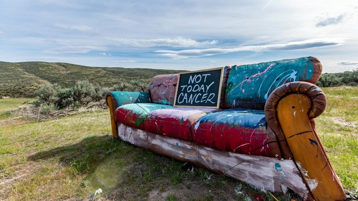 A vibrant painted couch outdoors with a 'Not Today Cancer' sign, symbolizing resilience.