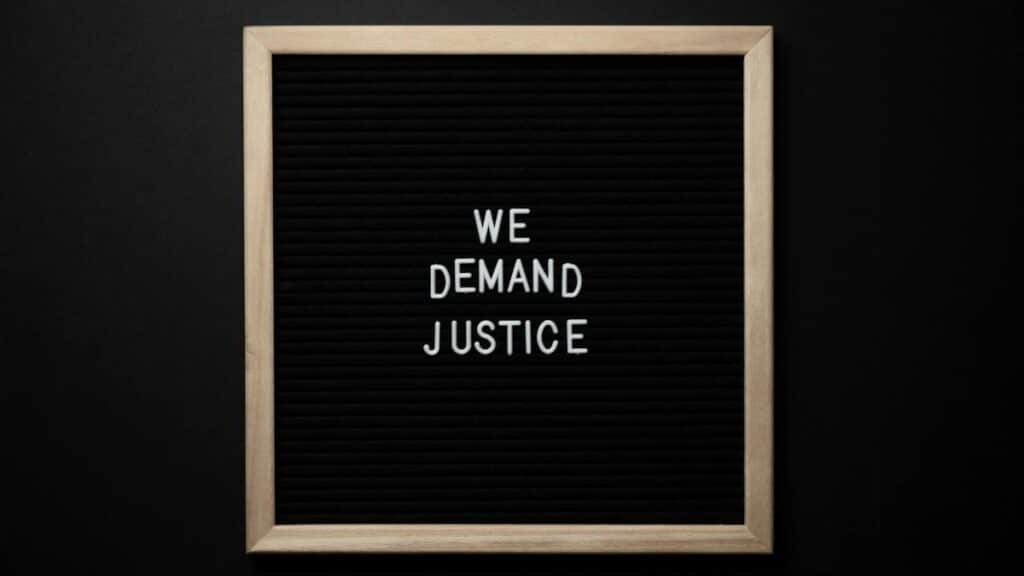 Sleek protest sign with 'We Demand Justice' text on black felt board. Minimalist design.