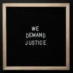 Sleek protest sign with 'We Demand Justice' text on black felt board. Minimalist design.