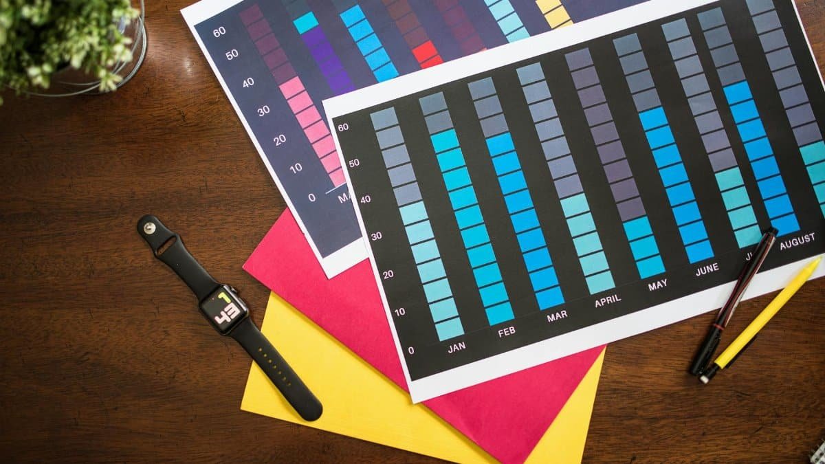 Flat lay of colorful business charts with a smartwatch, pens, and documents on a table.