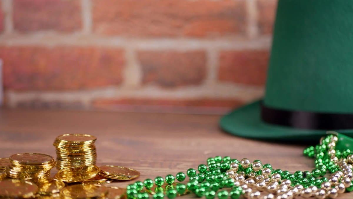Close-up of gold coins, green beads, and a green hat on a wooden table, ideal for St. Patrick's Day themes.